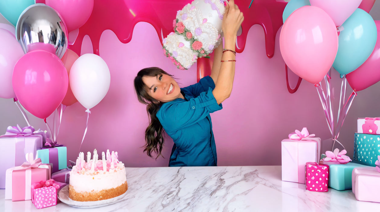 Nina con un pastel en fondo rosa con globlos y regalos a los lados